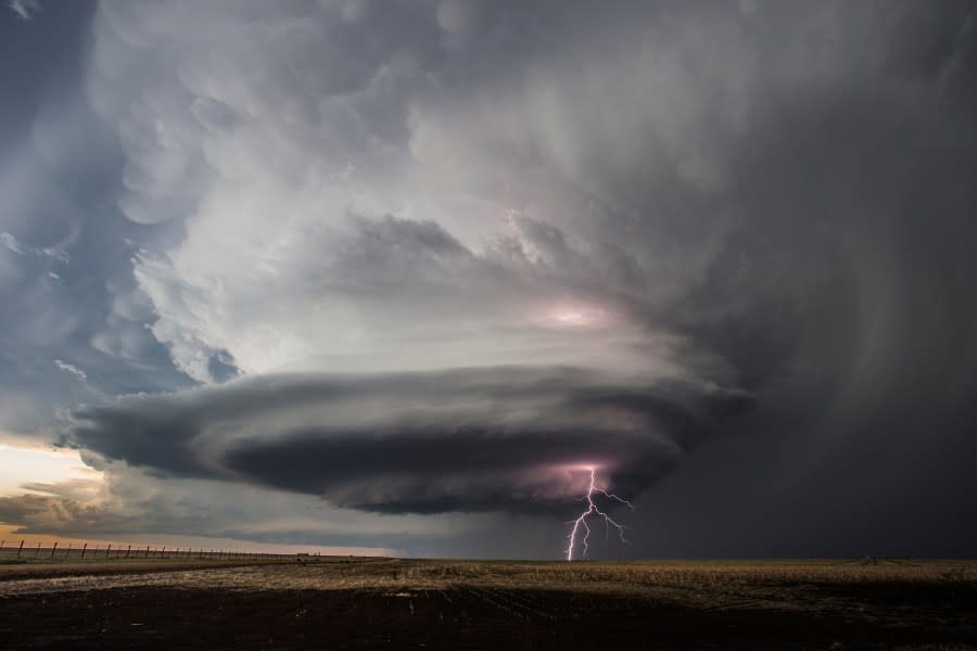 Supercell thunderstorm approaching a rural area with vivid lightning.